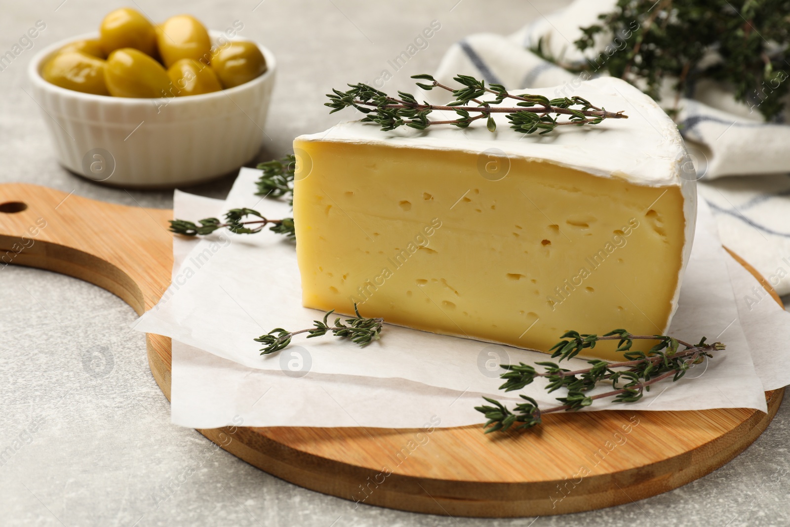 Photo of Piece of tasty camembert cheese and thyme on grey textured table, closeup