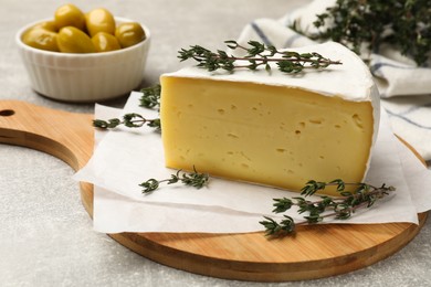 Photo of Piece of tasty camembert cheese and thyme on grey textured table, closeup