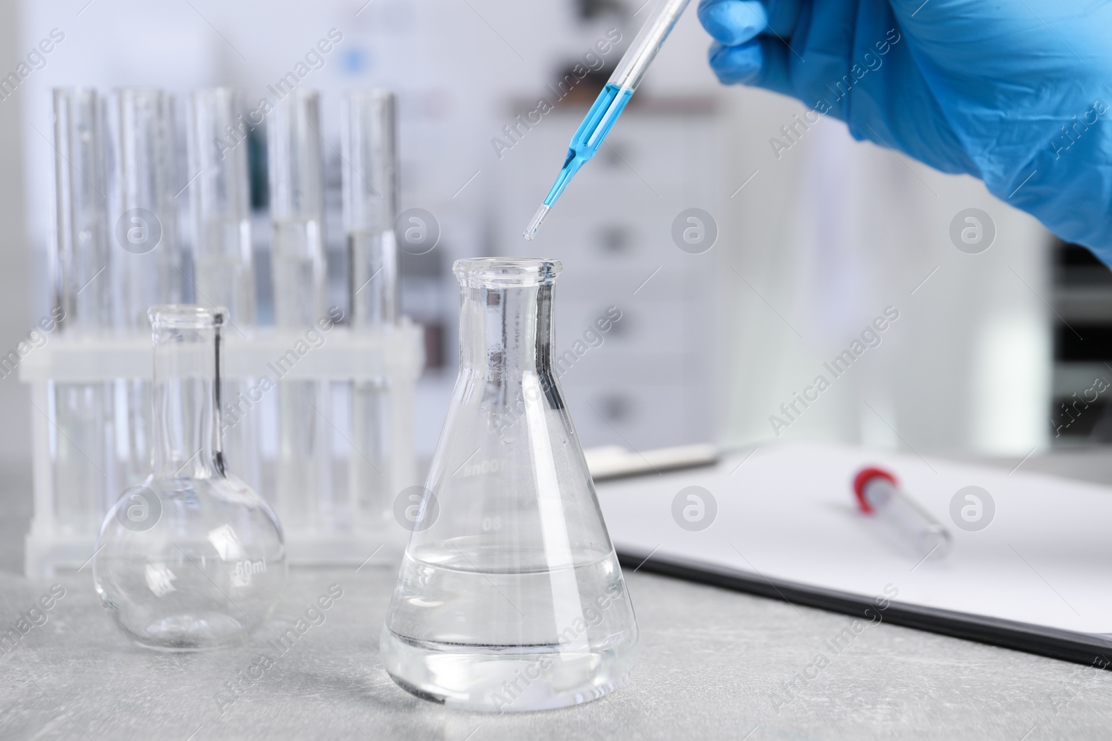 Photo of Laboratory analysis. Woman dripping liquid into flask at light grey table, closeup