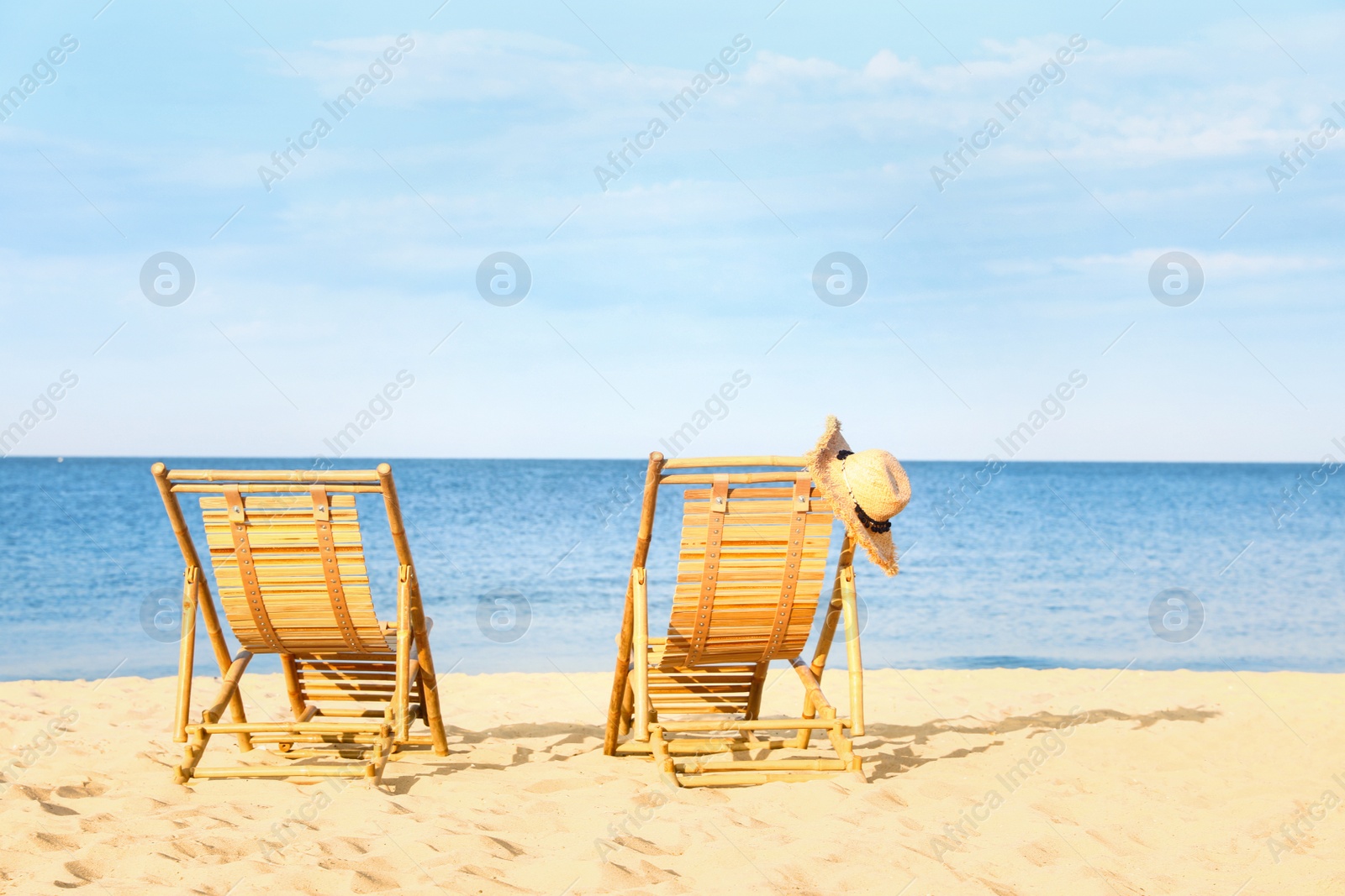 Photo of Empty wooden sunbeds with hat on sandy shore. Beach accessories