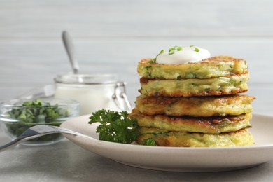 Photo of Delicious zucchini fritters with sour cream on grey table