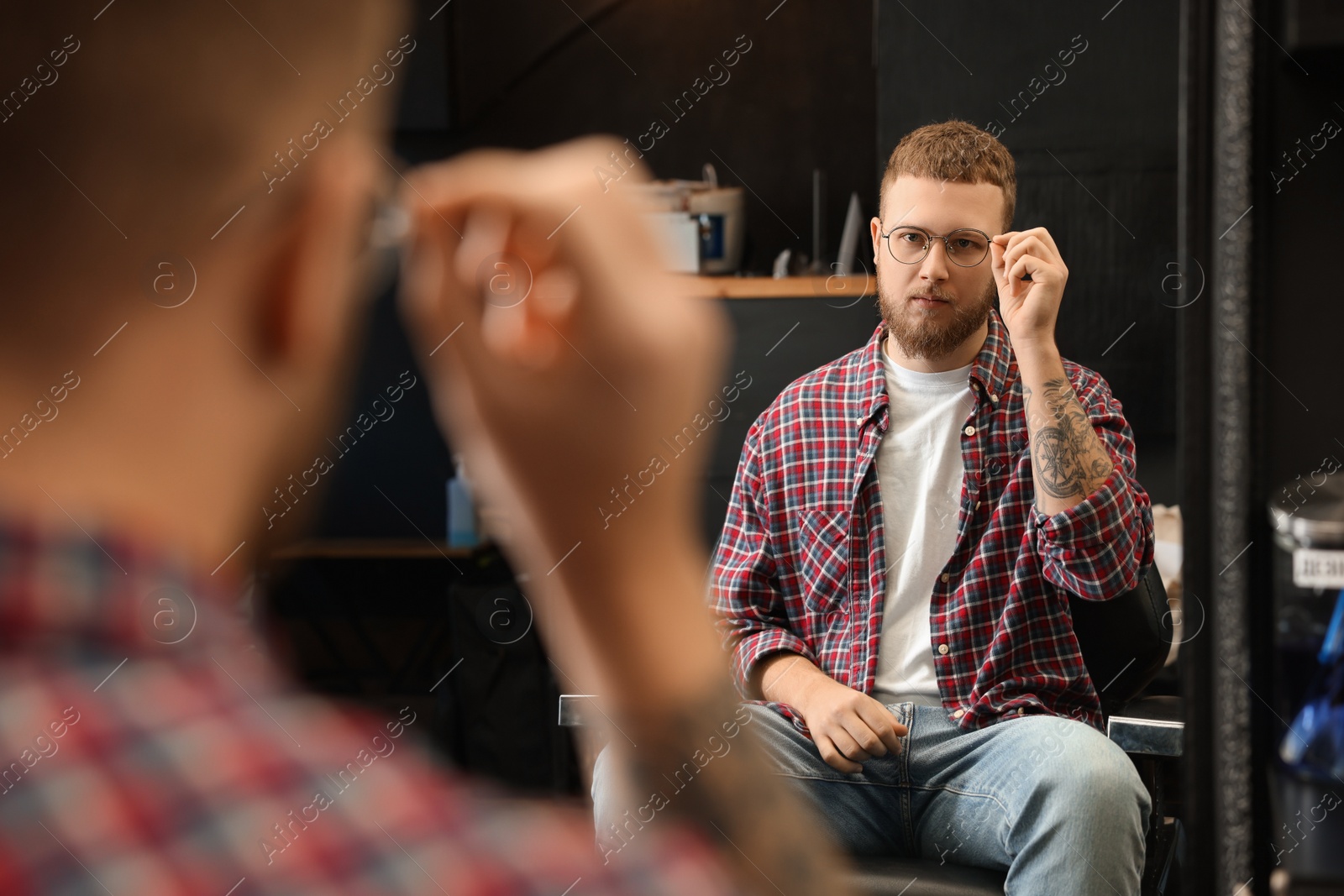 Photo of Young bearded man near mirror in barbershop