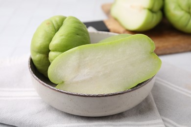 Photo of Cut and whole chayote in bowl on table, closeup