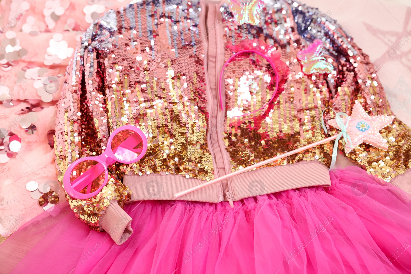 Photo of Stylish carnival costume with sequins, sunglasses, headband and wand on pink fabric, above view