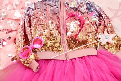 Photo of Stylish carnival costume with sequins, sunglasses, headband and wand on pink fabric, above view
