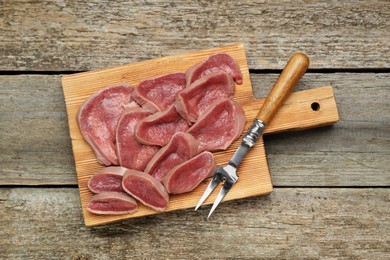 Photo of Board with slices of raw beef tongue on wooden table, top view