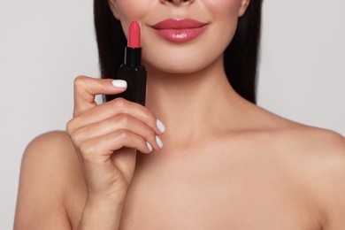 Photo of Young woman with beautiful makeup holding glossy lipstick on light gray background, closeup