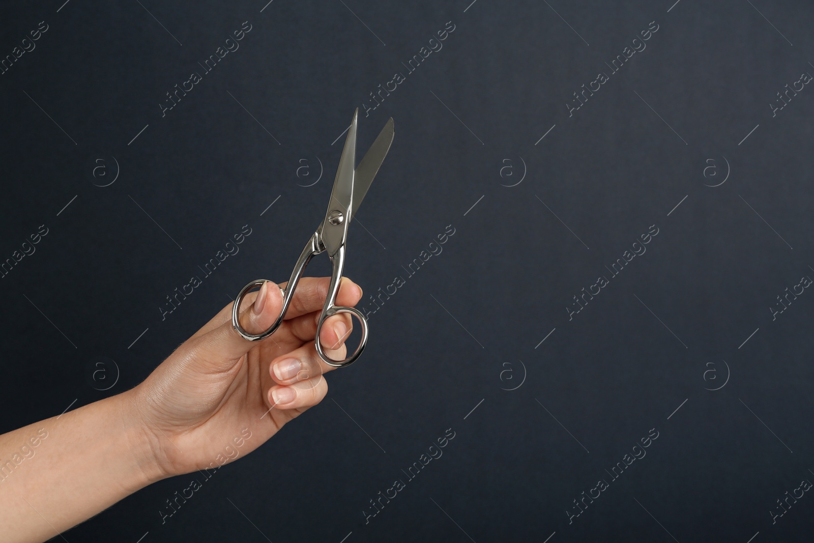 Photo of Woman holding sewing scissors on black background, closeup. Space for text