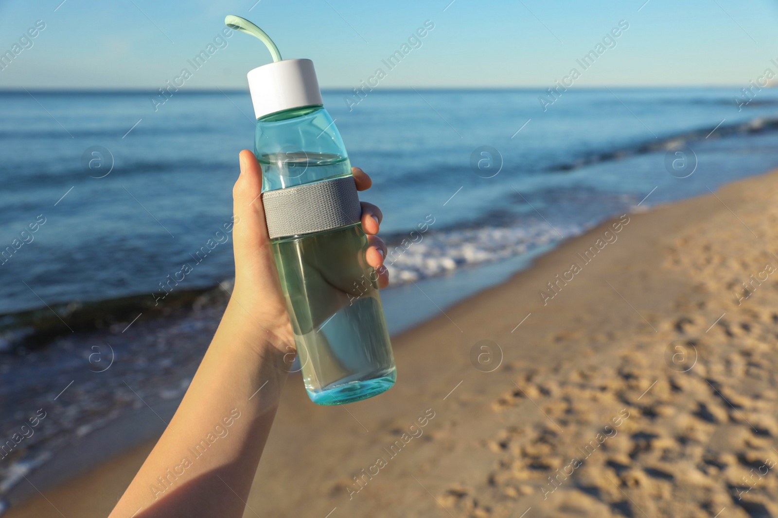 Photo of Woman holding glass bottle with water near sea, closeup. Space for text