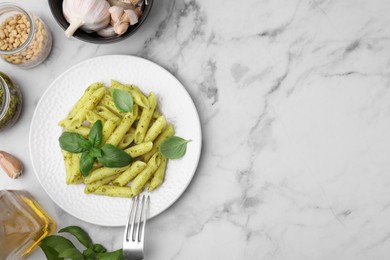 Photo of Delicious pasta with pesto sauce and ingredients on white marble table, flat lay. Space for text
