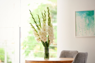 Photo of Vase with beautiful white gladiolus flowers on wooden table in room, space for text