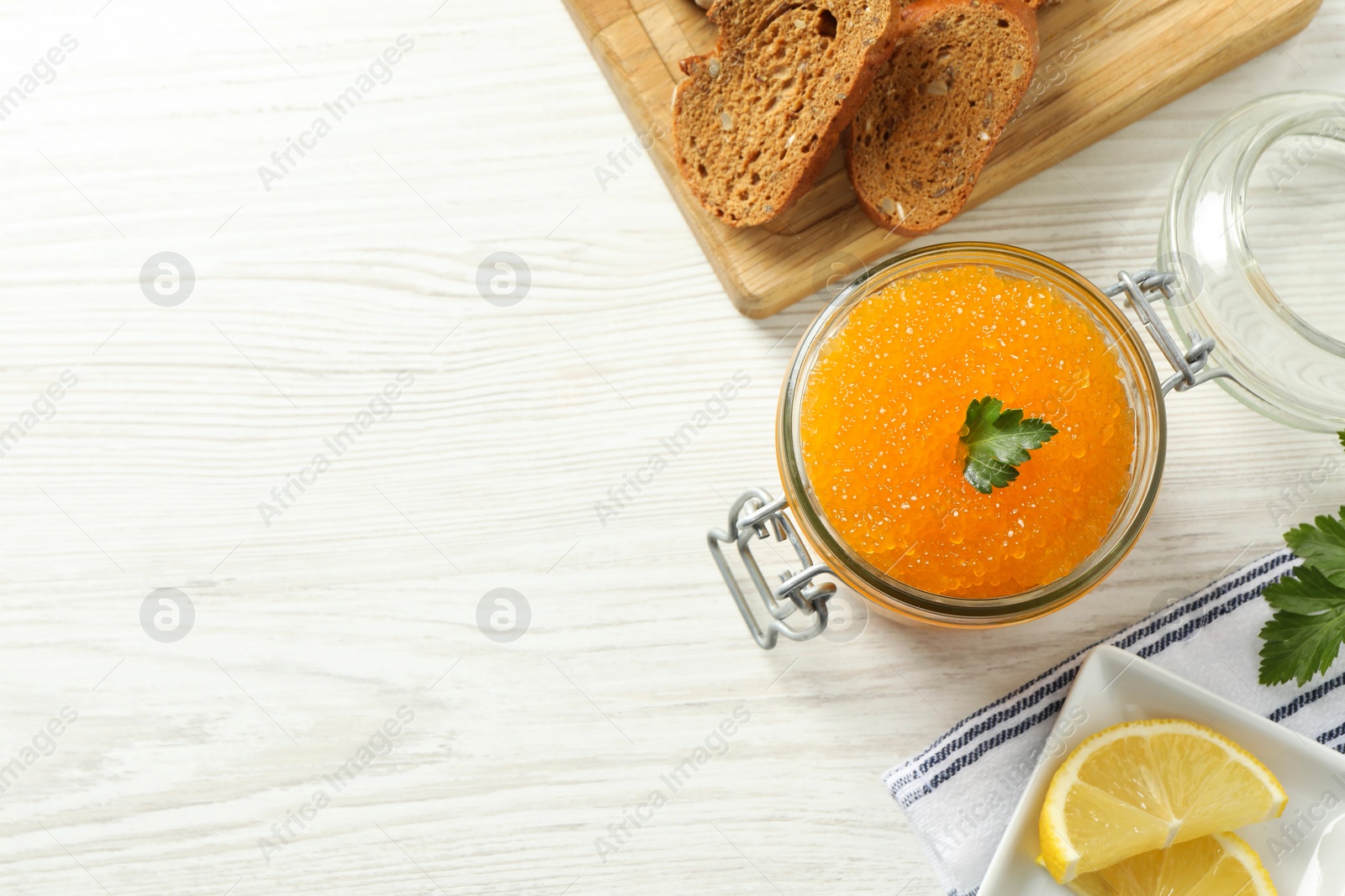 Photo of Fresh pike caviar in glass jar, bread and parsley on light wooden table, top view. Space for text