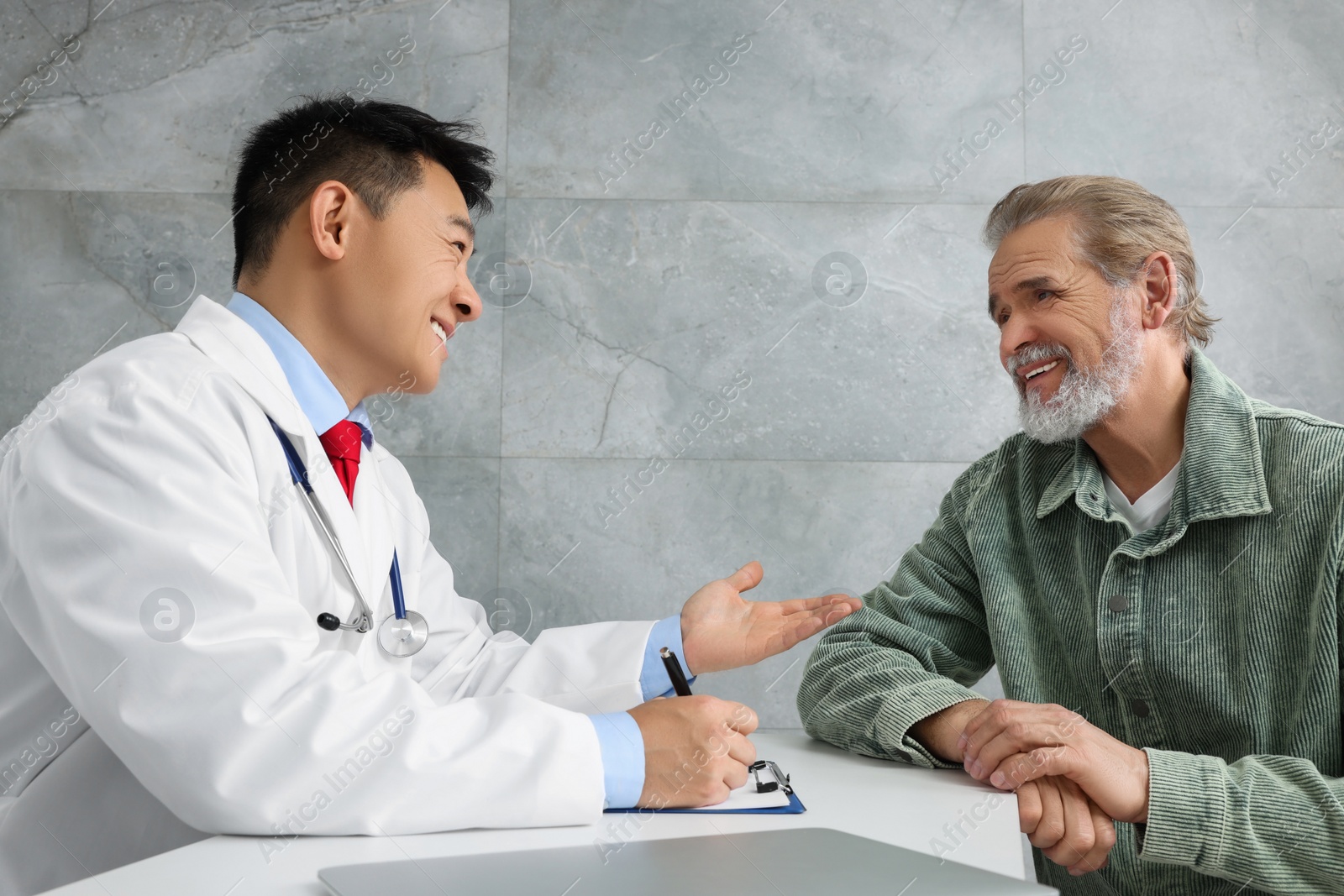 Photo of Doctor consulting senior patient at white table in clinic