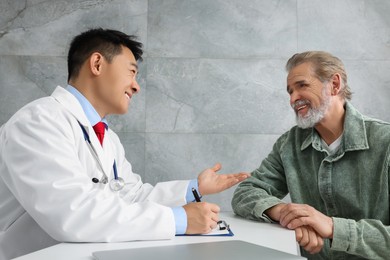 Photo of Doctor consulting senior patient at white table in clinic