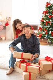 Photo of Young woman surprising her boyfriend with Christmas gift at home
