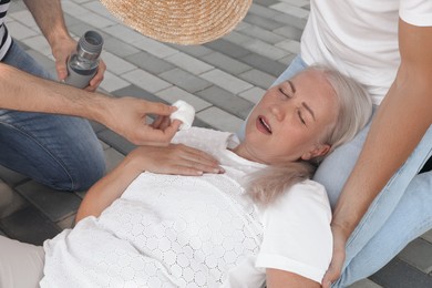 Men helping mature woman outdoors. Suffering from heat stroke