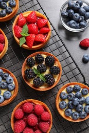 Tartlets with different fresh berries on grey table, flat lay. Delicious dessert