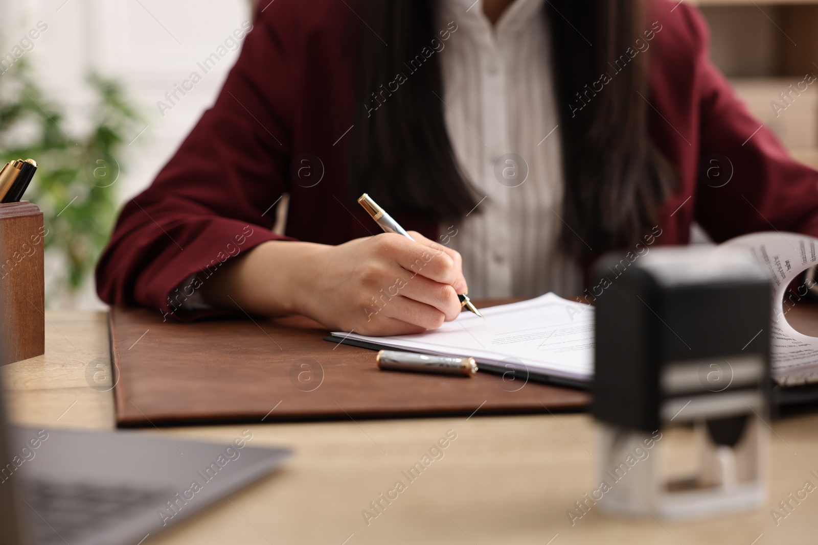 Photo of Notary signing document at table in office, closeup