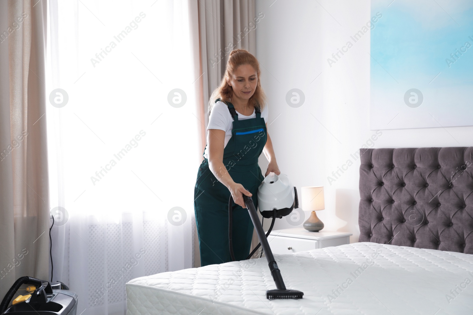 Photo of Janitor cleaning mattress with professional equipment in bedroom