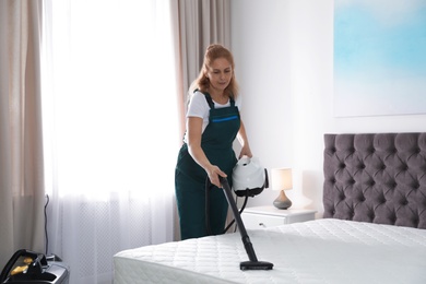 Photo of Janitor cleaning mattress with professional equipment in bedroom