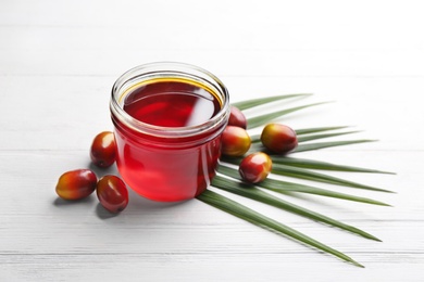 Palm oil in glass jar, tropical leaf and fruits on white wooden table