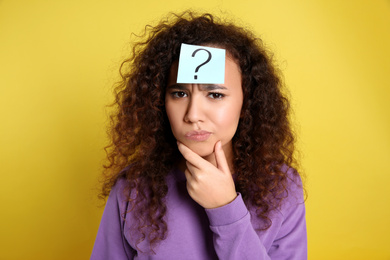 Photo of Emotional African-American woman with question mark sticker on forehead against yellow background
