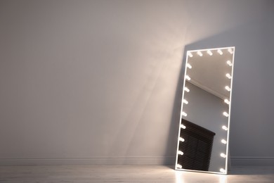 Photo of Stylish mirror with light bulbs near white wall indoors. Interior element