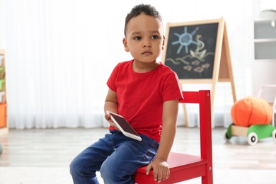 Photo of Cute little African-American child playing on mobile phone in kindergarten. Indoor activity