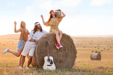 Photo of Happy hippie friends with radio receiver and guitar in field, space for text