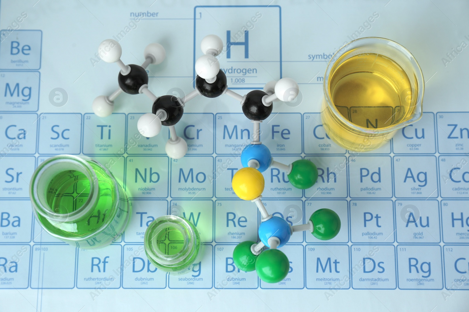 Photo of Molecular model and laboratory glassware with liquid on periodic table, flat lay