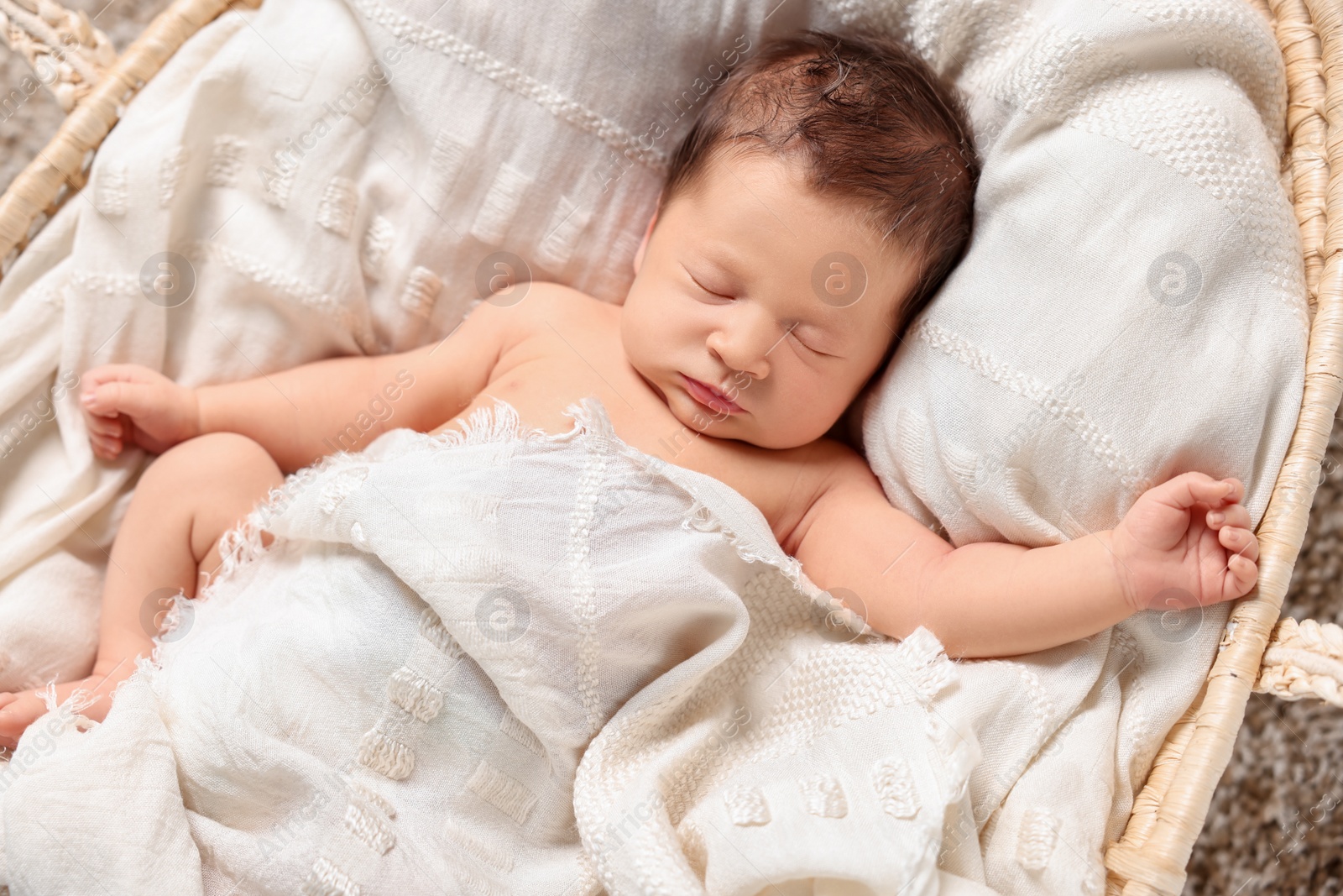 Photo of Cute newborn baby sleeping on white blanket in wicker crib