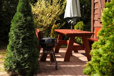 Photo of Wooden furniture and modern barbecue grill near green trees