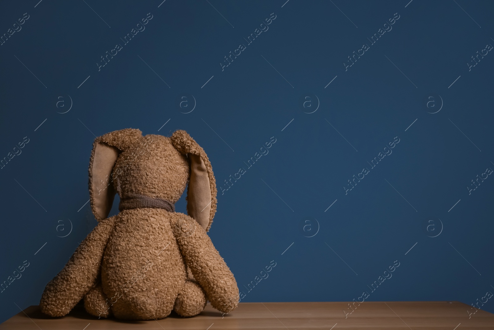 Photo of Abandoned toy bunny on table against dark background. Time to visit child psychologist