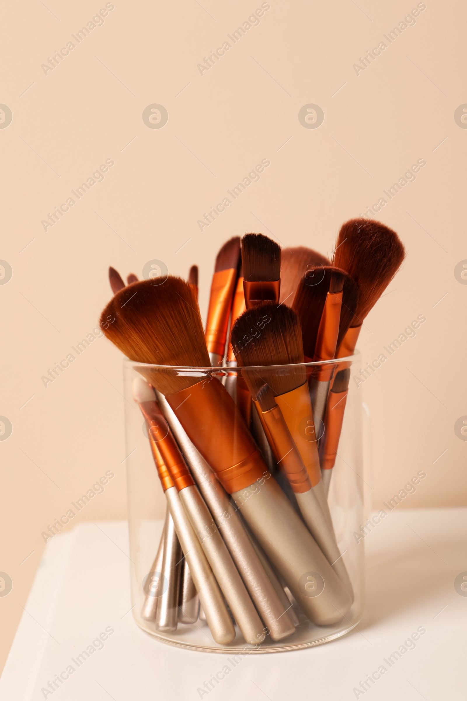 Photo of Set of professional makeup brushes on white table against beige background