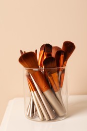 Photo of Set of professional makeup brushes on white table against beige background