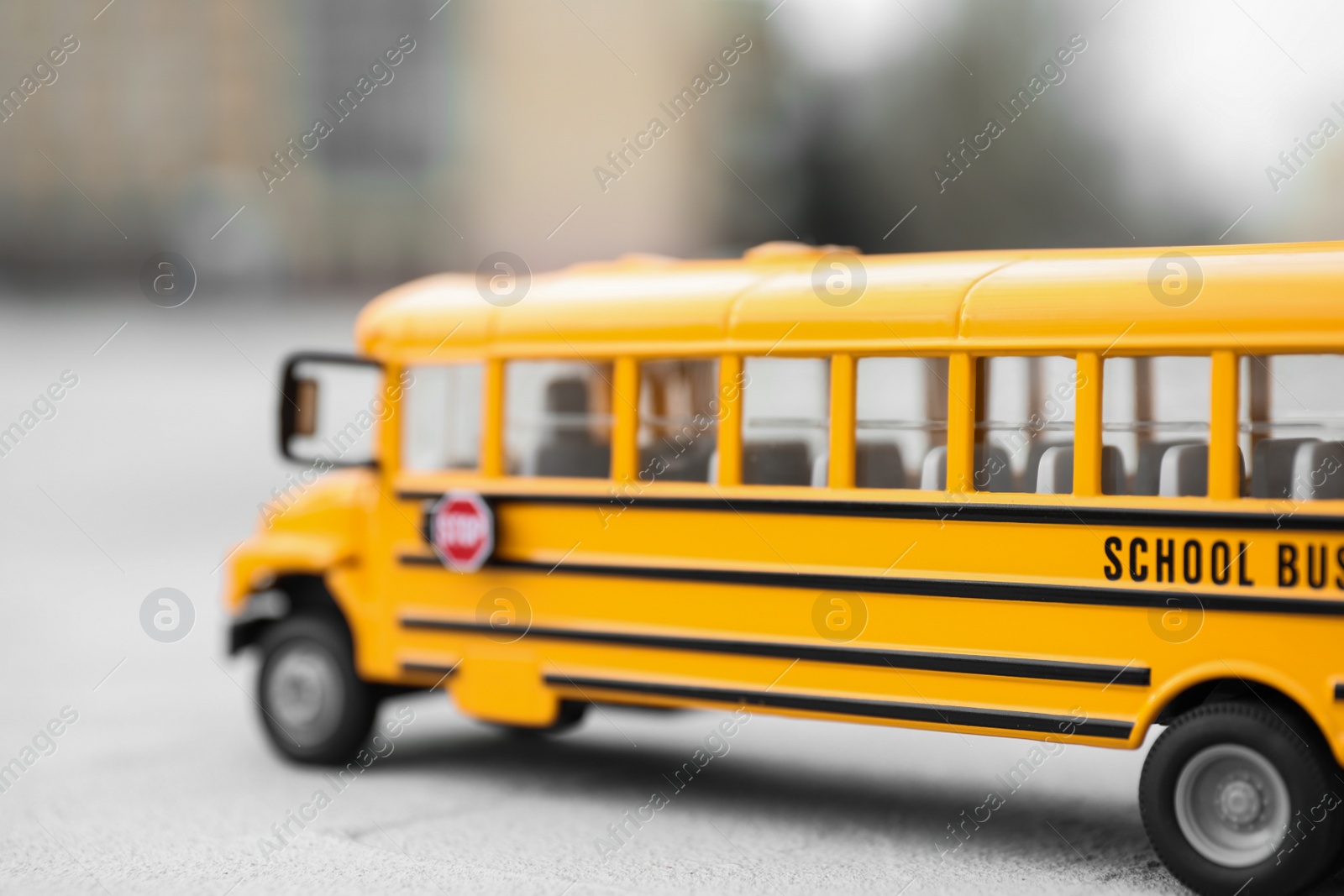 Photo of Yellow toy school bus against blurred background, closeup. Transport for students