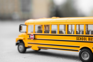 Yellow toy school bus against blurred background, closeup. Transport for students