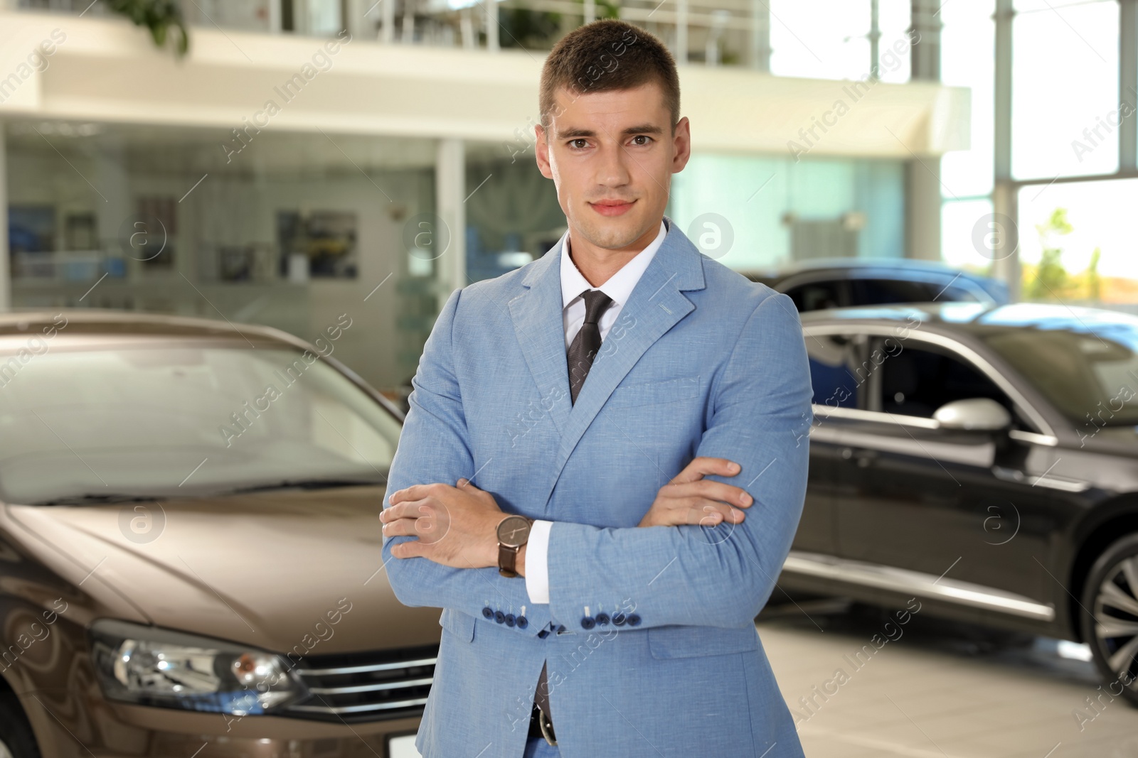 Photo of Young salesman near new car in modern dealership