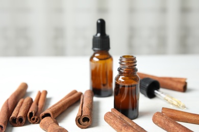 Photo of Bottles of essential oils and cinnamon sticks on white wooden table