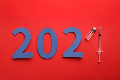 Photo of Paper numbers, syringe and vial with coronavirus vaccine forming 2021 on red background, flat lay