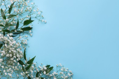 Photo of Beautiful gypsophila flowers and green leaves on light blue background, flat lay. Space for text