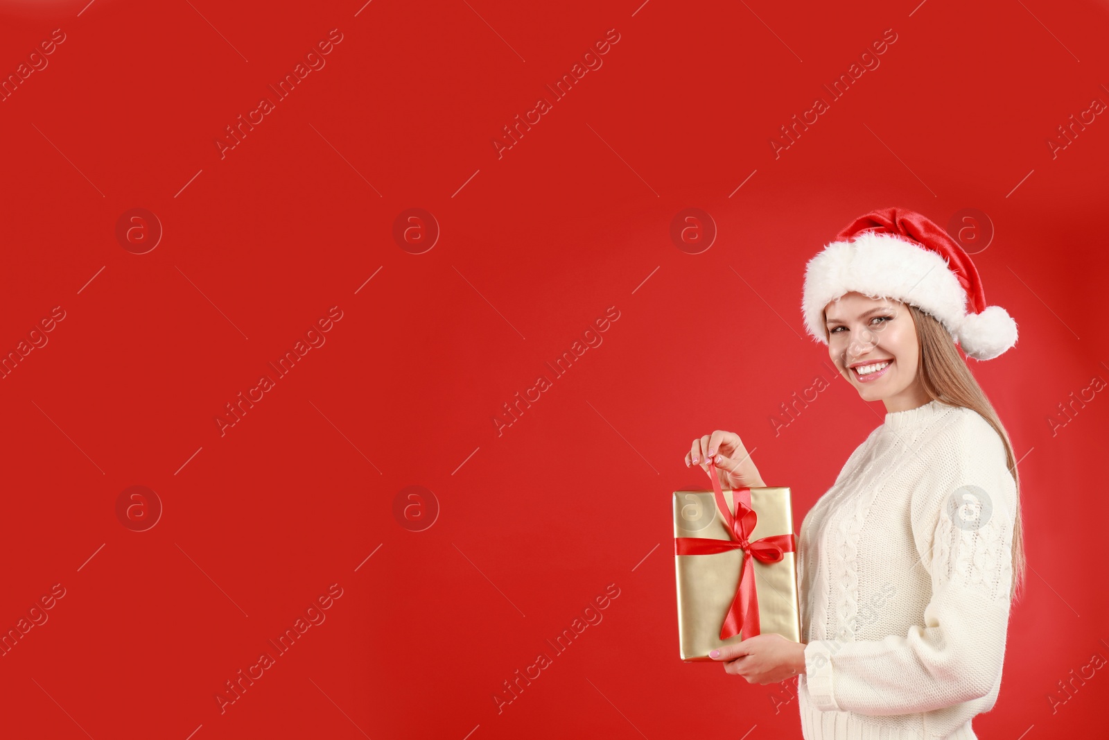 Photo of Happy young woman in Santa hat with Christmas gift on red background. Space for text