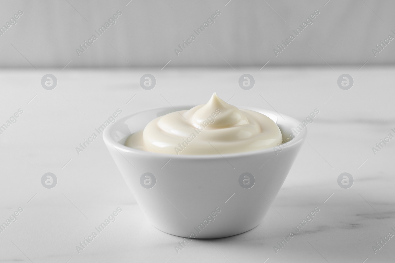 Photo of Tasty mayonnaise sauce in bowl on white table, closeup