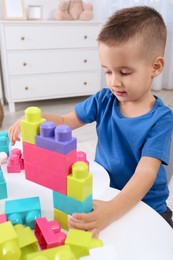 Cute little boy playing with colorful building blocks at table in room