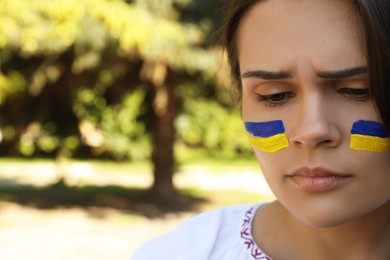 Sad young woman with drawings of Ukrainian flag on face outdoors, closeup. Space for text