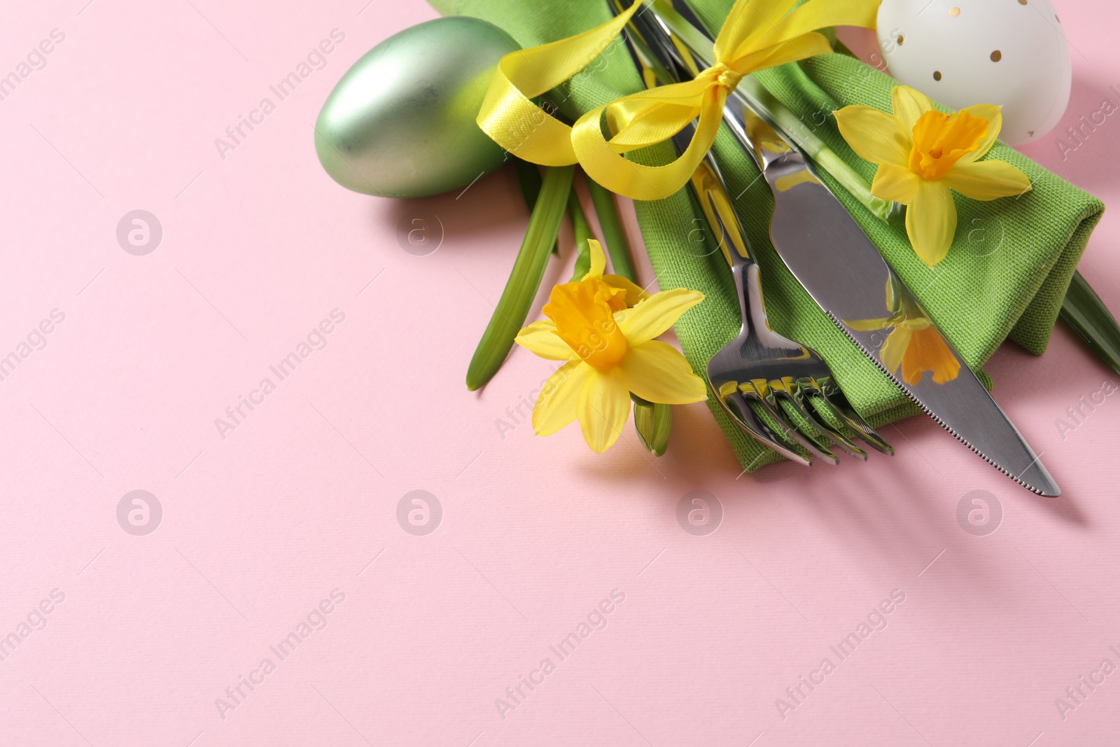 Photo of Cutlery set, Easter eggs and narcissuses on pale pink background, space for text. Festive table setting