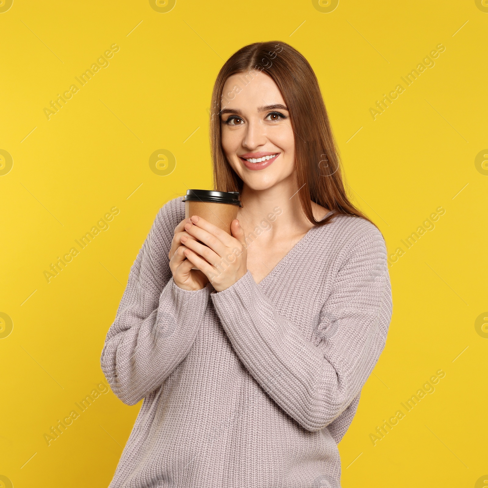 Photo of Beautiful young woman in sweater with drink on yellow background. Winter season