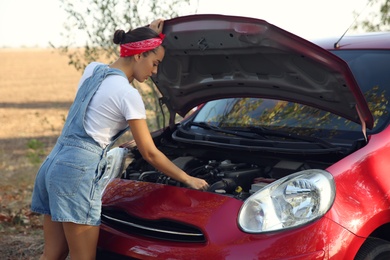 Photo of Stressed young woman fixing broken car outdoors