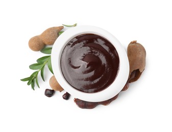 Photo of Bowl of tasty tamarind sauce, leaves and fresh pods isolated on white, top view