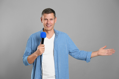 Male journalist with microphone on grey background